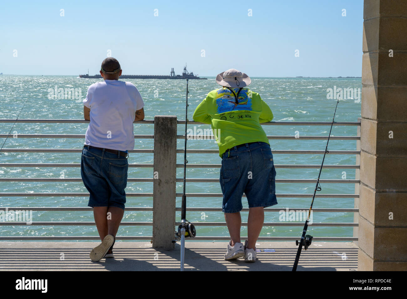 Fort De Soto Park, Florida -- February 17, 2019. Two fishermen on a pier pause to watch a large ship go by. Stock Photo