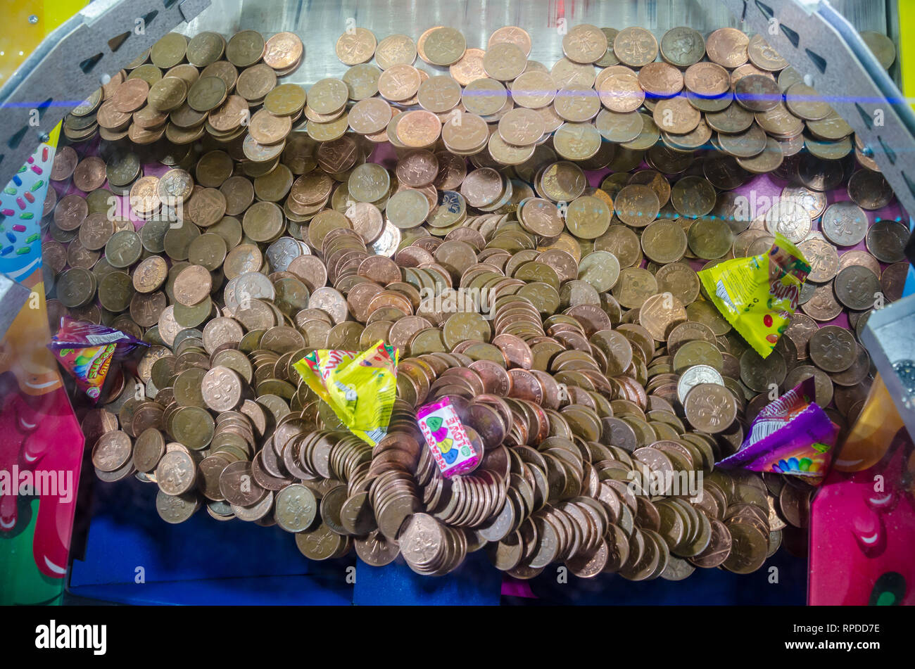 A two penny falls game where two pence piece coins balance precariously on the edge of a lower shelf waiting to be knocked off and won. Stock Photo