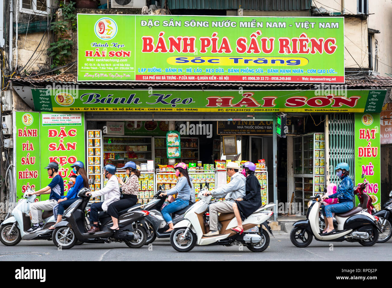 Commuters on scooters and motorcycles travelling passed as local grocery shop, Ha Noi, Viet Nam, Asia Stock Photo