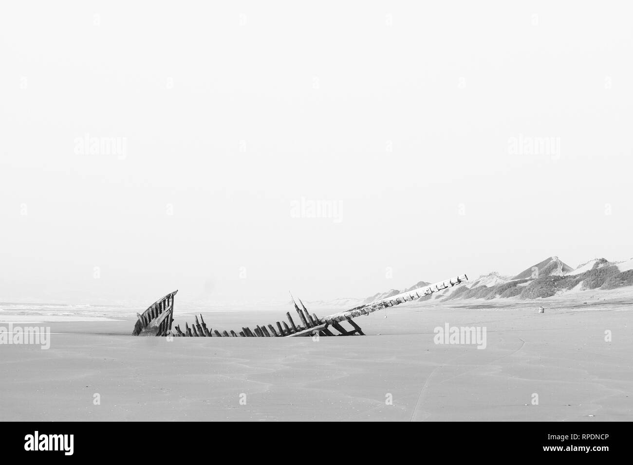 Monochromatic, black and white, panorama of a wide empty beach, Atlantic Ocean, wooden ship wreck, abandoned  boat. Solitude seascape background. Stock Photo