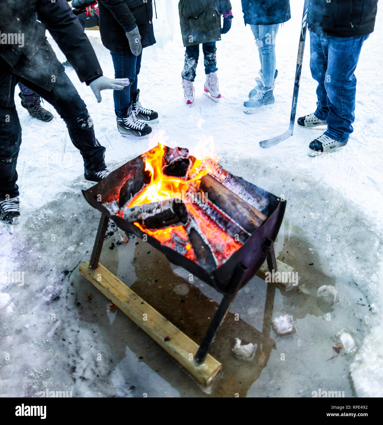 People warming up around an outdoor fire pit, wearing ice skates at The Forks, Winnipeg, Manitoba, Canada. Stock Photo