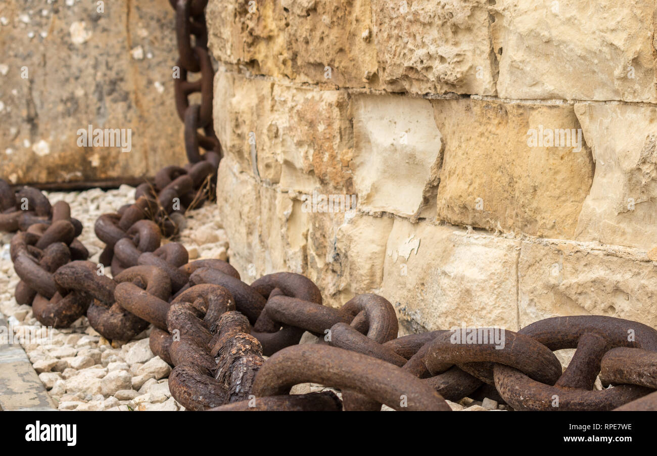 A huge, old and rusty chain hanging down from sandstone wall in Fort St