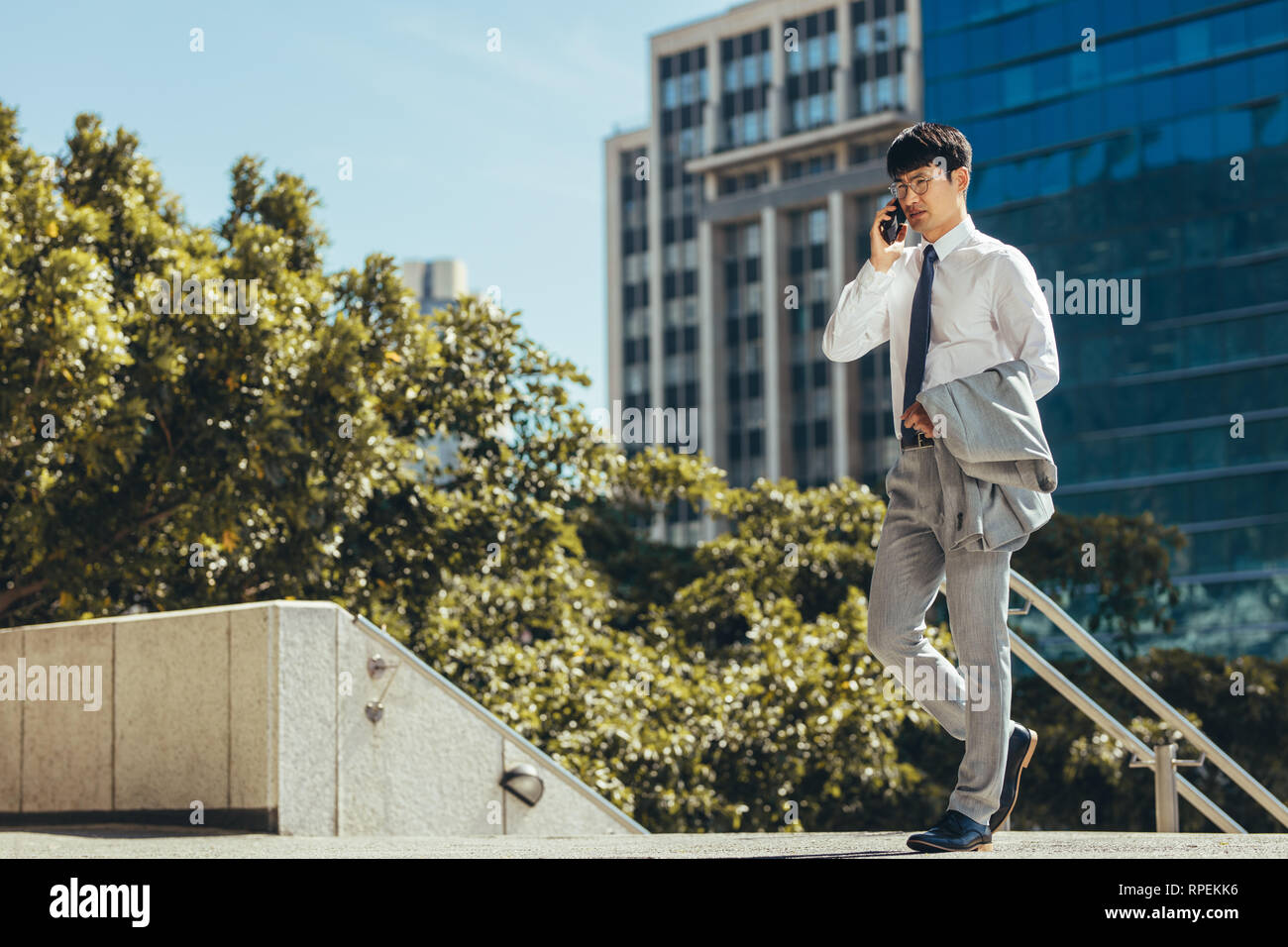 businessman talking on his cell phone while walking outdoors. Man making a phone call against a office building in background. Stock Photo
