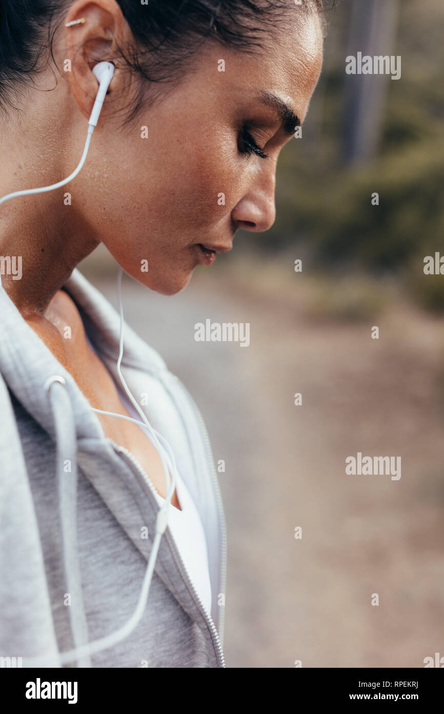Healthy young woman with sweat standing outdoors after her workout. Tired fitness female resting after exercising outdoors. Stock Photo