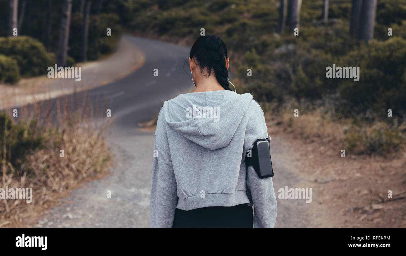 Rear view shot of young woman walking on country trail. Fitness woman ...