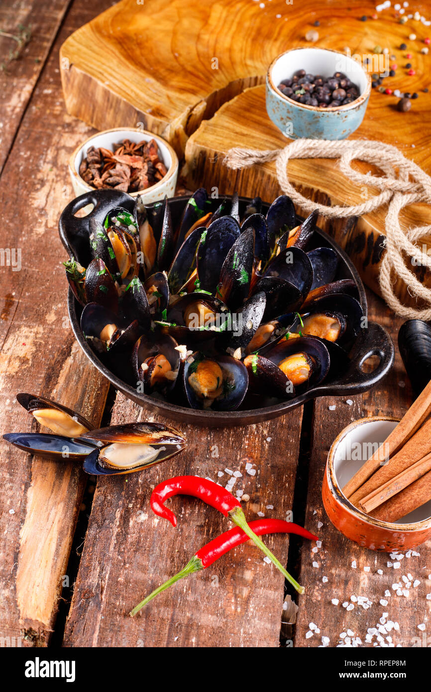 Boiled mussels in copper dish for cooking on wooden background, near rope and products for cooking close-up Stock Photo