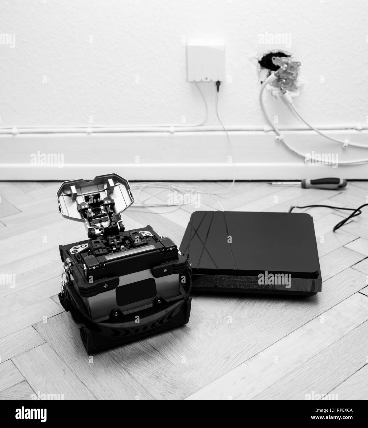 FTTH fiber installation at home with new arc clad-alignment fusion splicer used for splicing an array of thin optical fiber types with CATV on wall socket and tv internet receiver tuner black and white Stock Photo