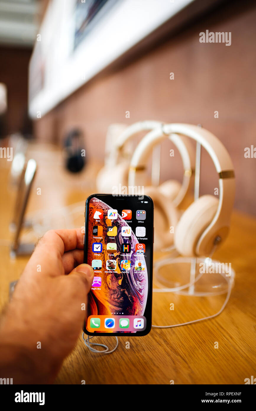 PARIS, FRANCE - OCT 26, 2018: Man hand holding new iphone Xs Xr Max with Apple Music app and multiple wireless bluetooth headphones Beats By Dr Dre Studio 3 phone home screen Stock Photo