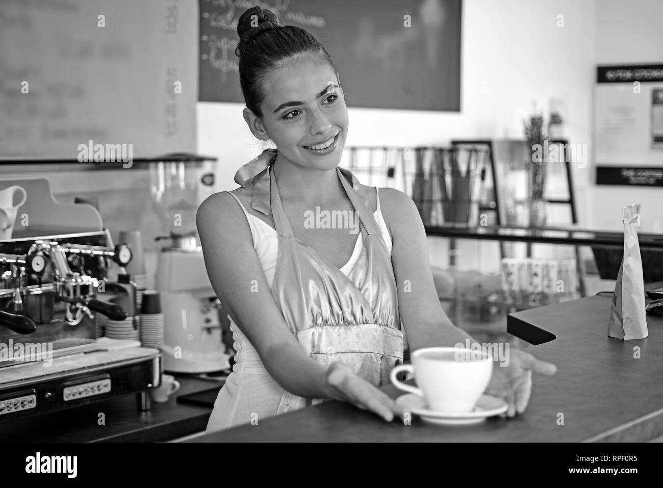 Todays good mood is sponsored by coffee. Woman barista in coffee shop. Barista serve cup of hot coffee drink with smile. Pretty woman stand behind Stock Photo