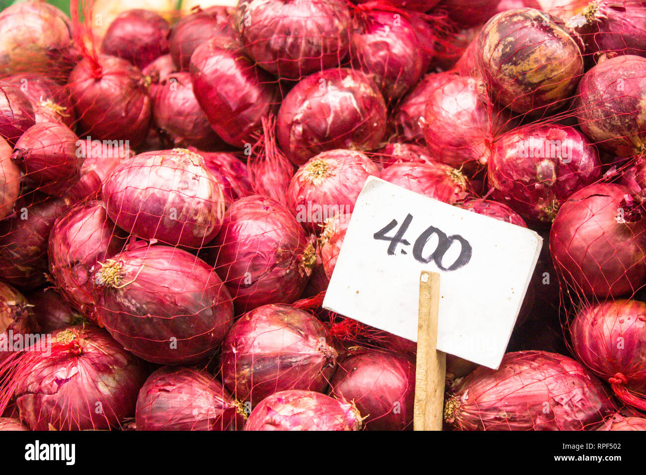 Red onions fresh and organic on sale at a vegetable stand in a food local market with the white price tag right side on wood stick. Stock Photo