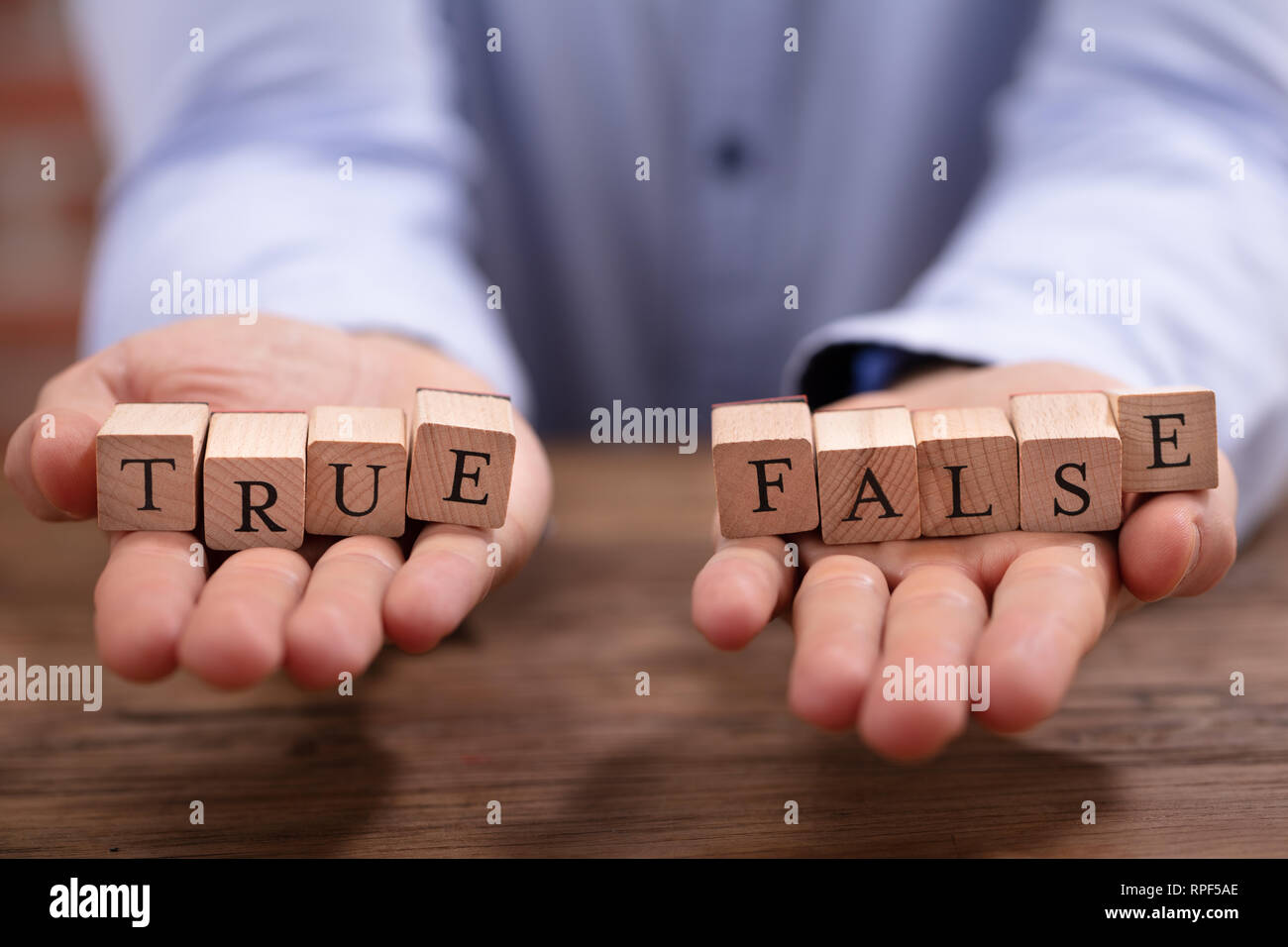 Close-up Businessman's Hand Holding True And False Blocks Over Wooden Desk Stock Photo