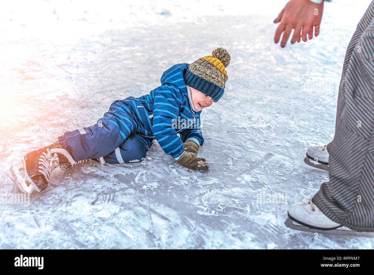 Little boy, 2-3 years old, winter uniform, blue overalls hat, fell on ice  skates. The concept of first lesson skating support and support, help of  Stock Photo - Alamy