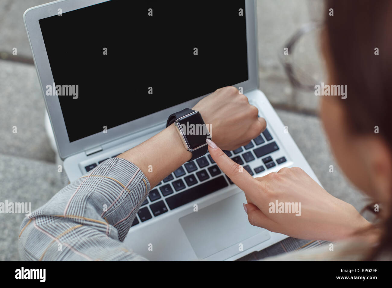 Time management. Young lady sitting on the city street checking time on watch back view close-up Stock Photo