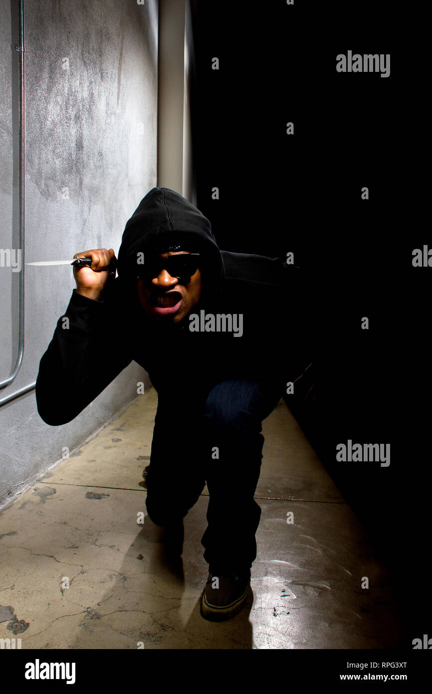 hooded criminal with a knife hiding in the shadows of a street alley