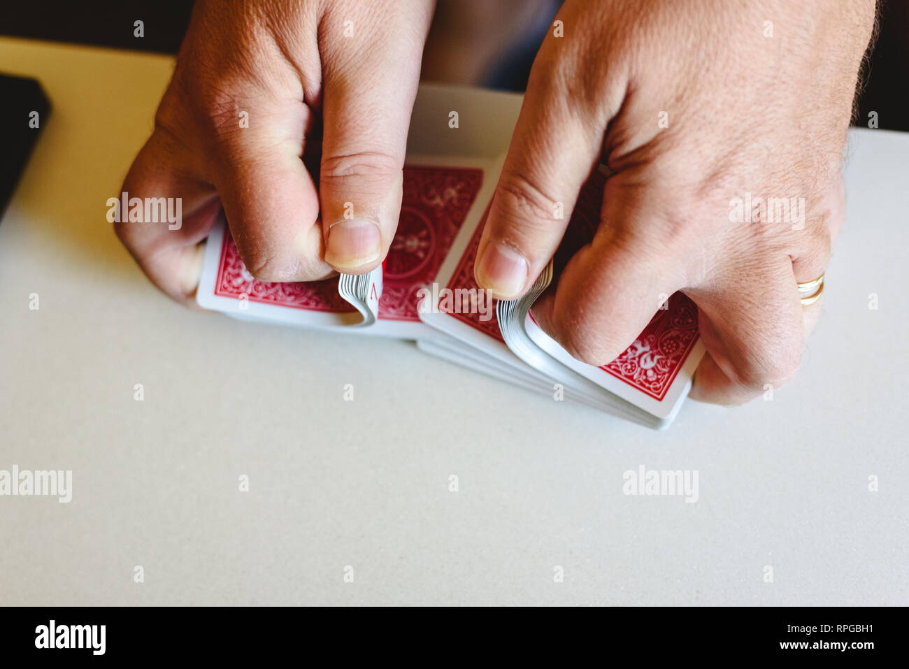 Hands of magician shuffling a deck of poker cards before doing a trick on a white table Stock
