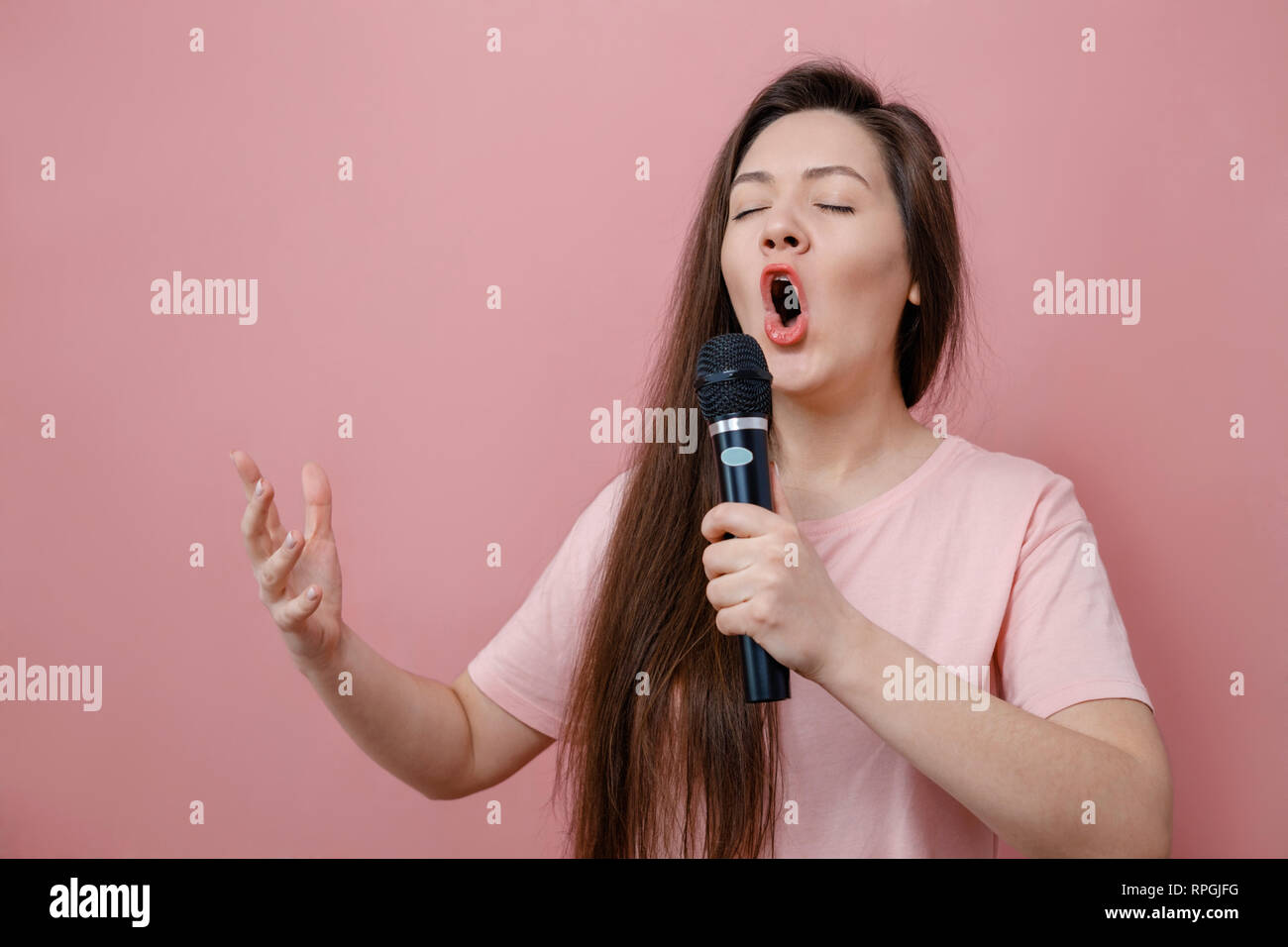 young woman with microphone in hand  on pink background sings like opera singer Stock Photo