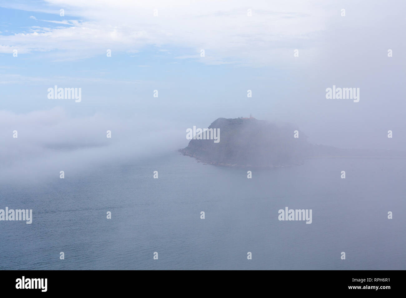 Small island with light house hidden under low mist and clouds over ocean Stock Photo