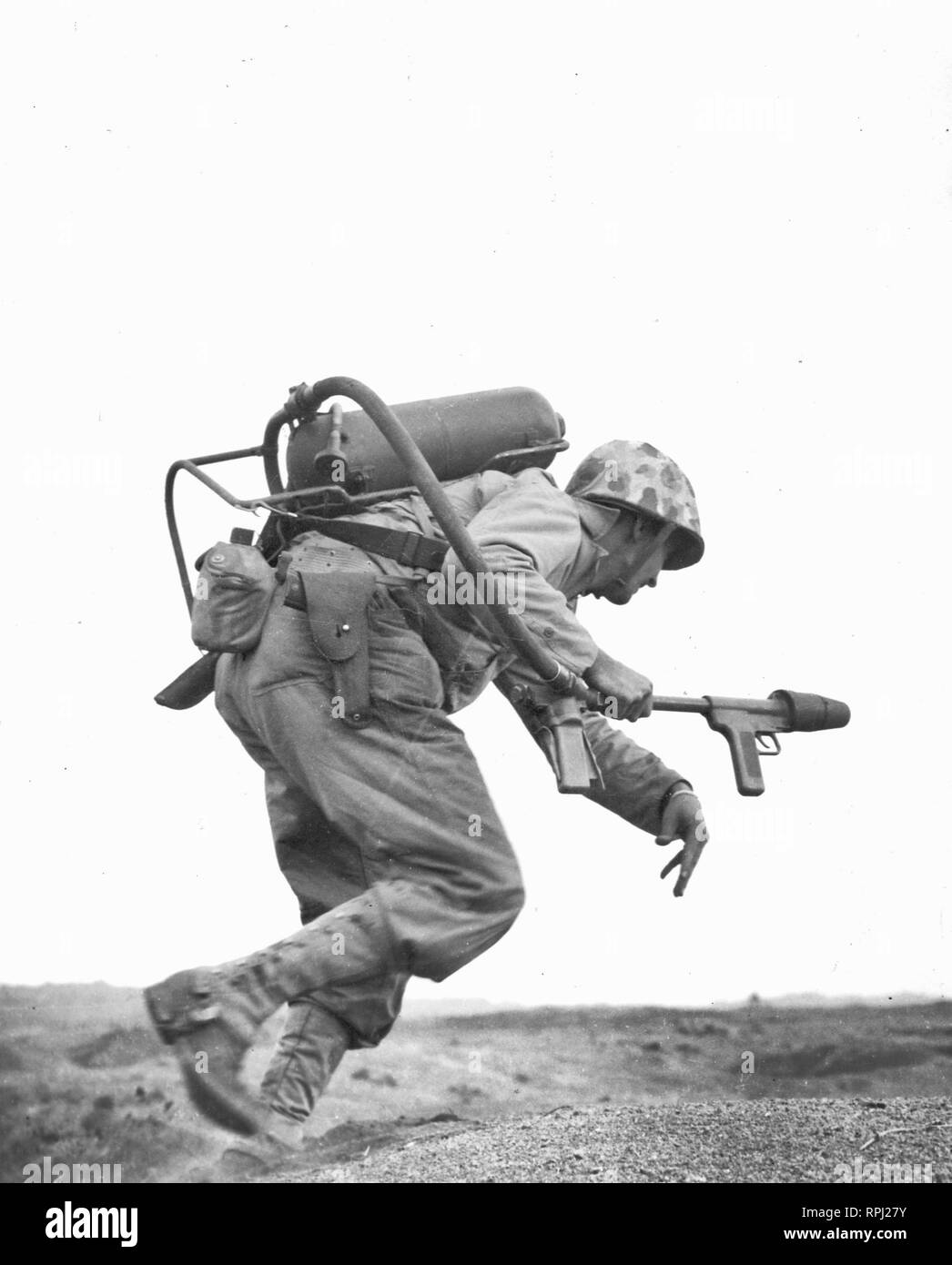 A flamethrower operator of Co. E, 2nd Bn, 9th Marines, runs under fire on Iwo Jima, February 1945. Stock Photo