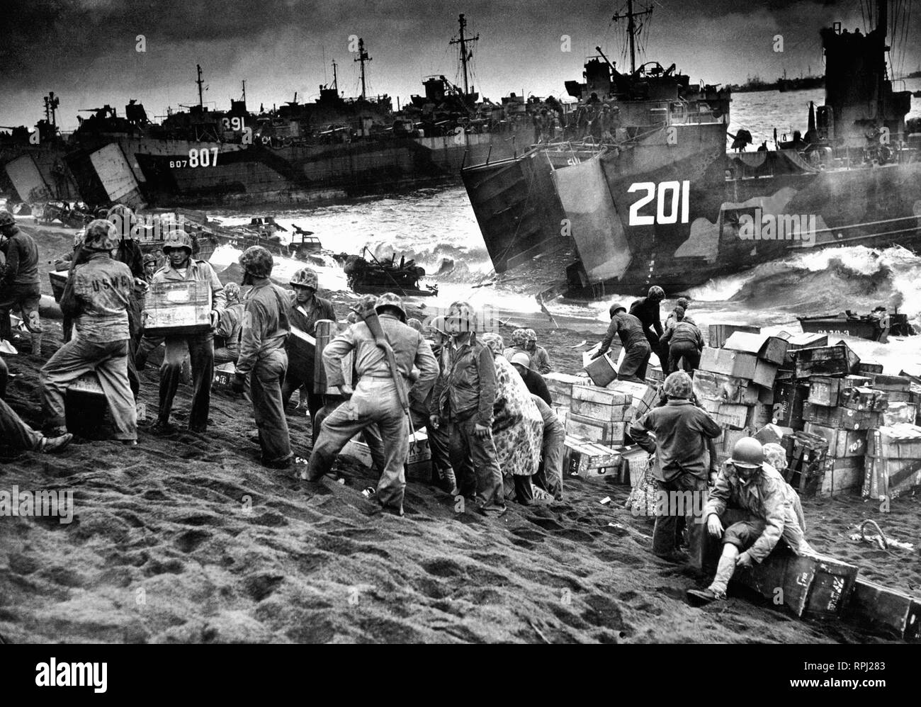 Out of the gaping mouths of Coast Guard and Navy Landing Craft, rose the great flow of invasion supplies to the blackened sands of Iwo Jima, a few hours after the Marines had wrested their foothold on the vital island. 1945. Stock Photo
