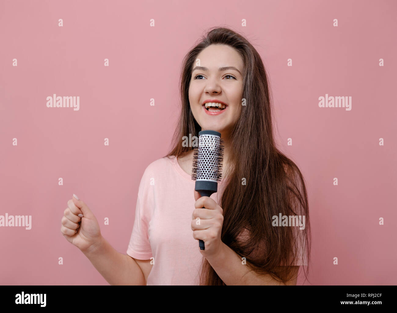 young woman with hairbrush like with microphone in hand on pink