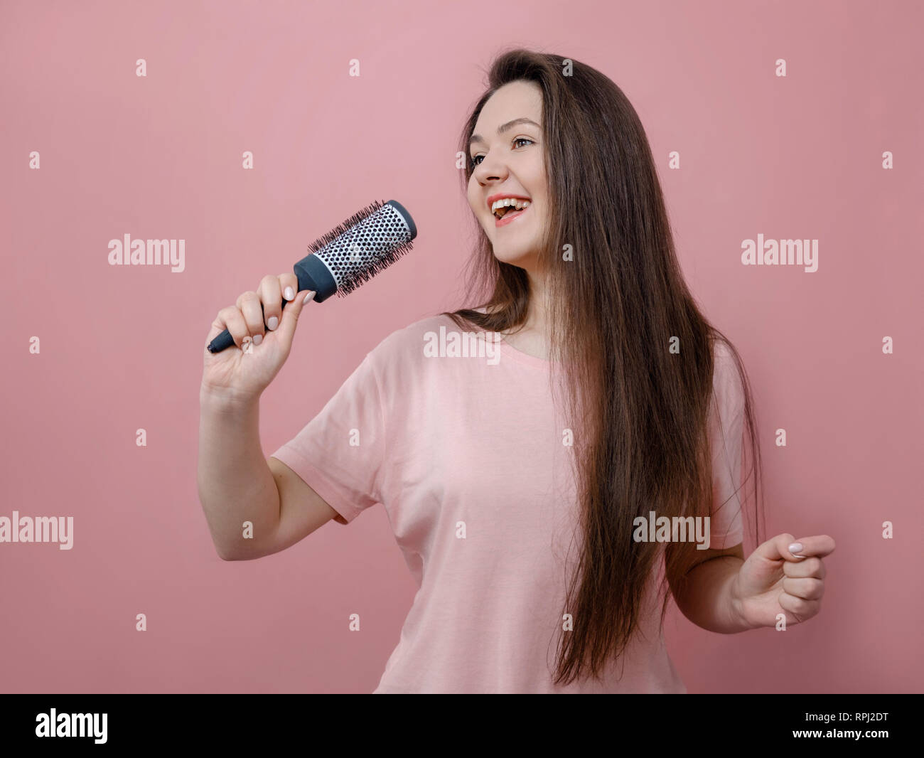 young woman with hairbrush like with microphone in hand on pink