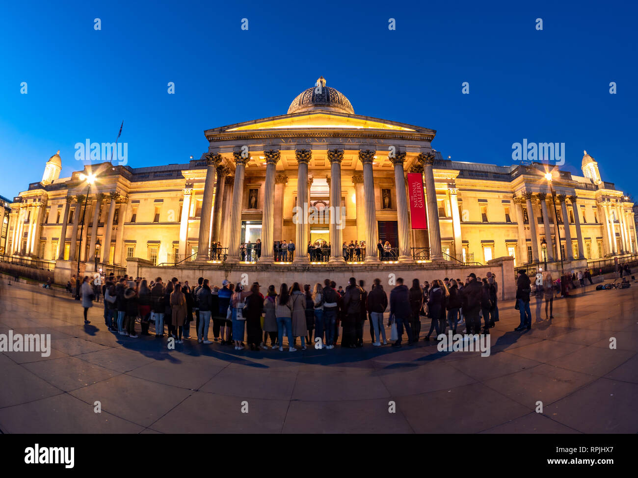 London, England, UK - February 15, 2019: Group of tourists watching a show in front of National Gallery of Art and Culture in Trafalgar Square in even Stock Photo
