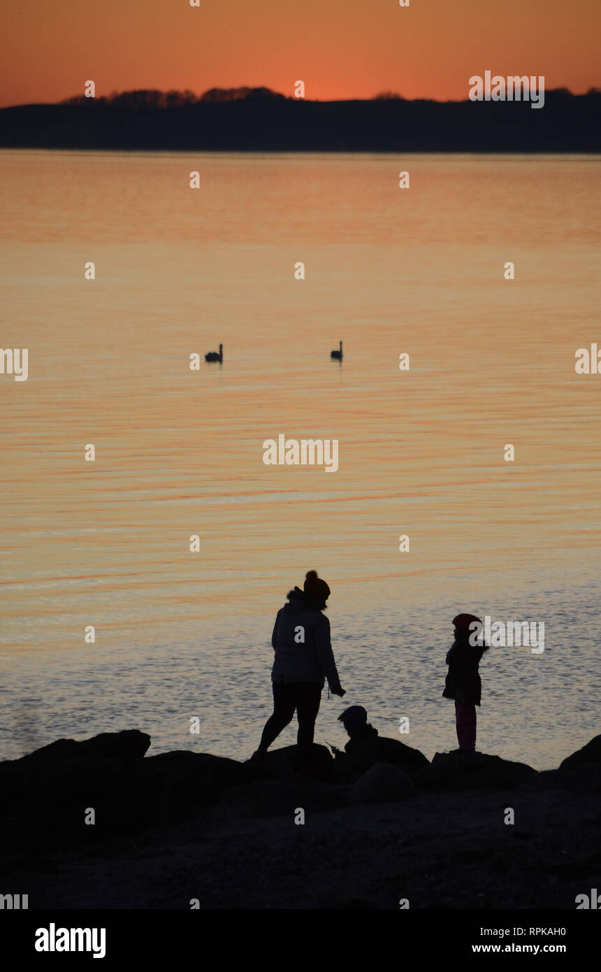 Sunset over the sea, people seen as black silhouettes towards the sea. Stock Photo