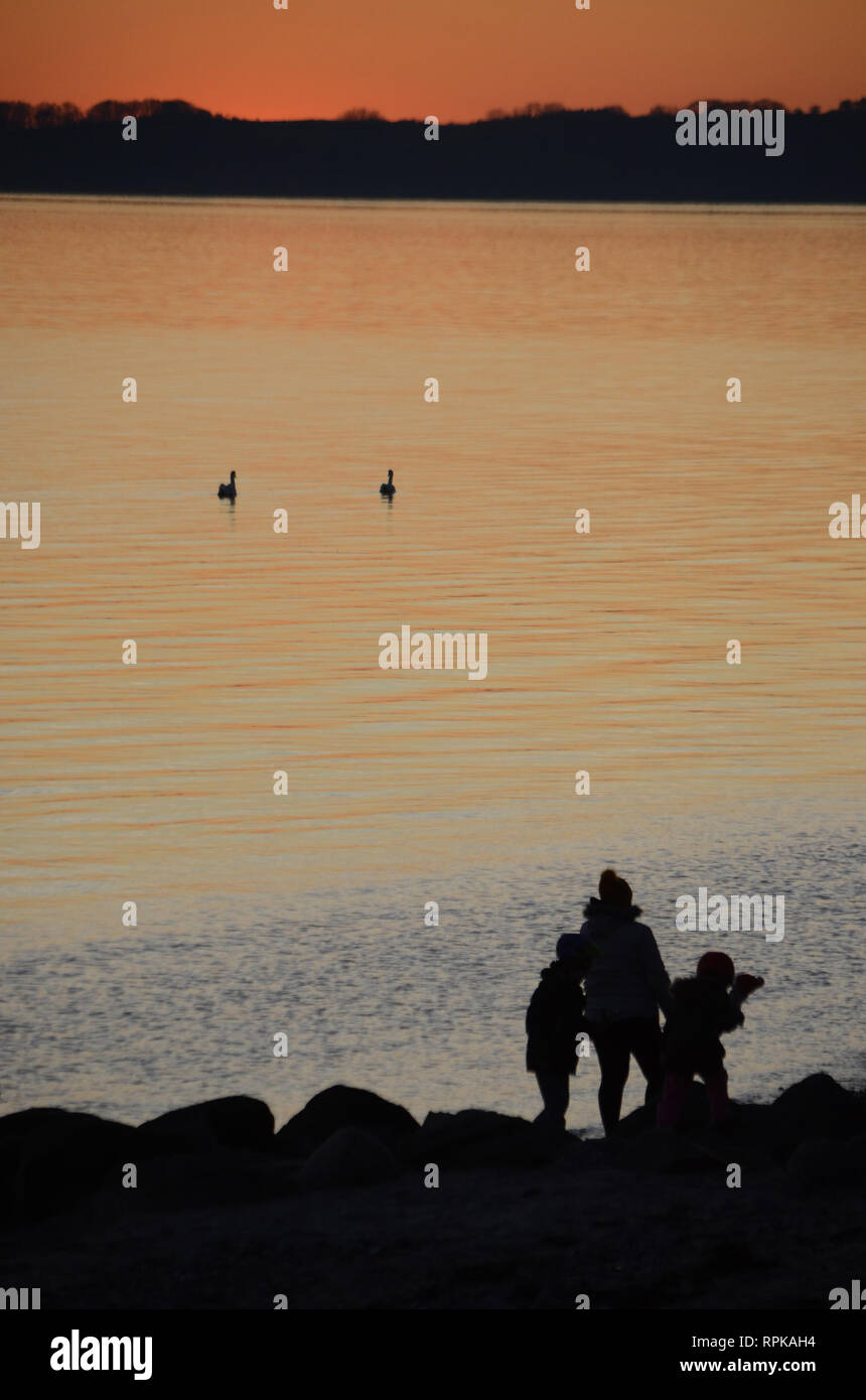 Sunset over the sea, people seen as black silhouettes towards the sea. Stock Photo