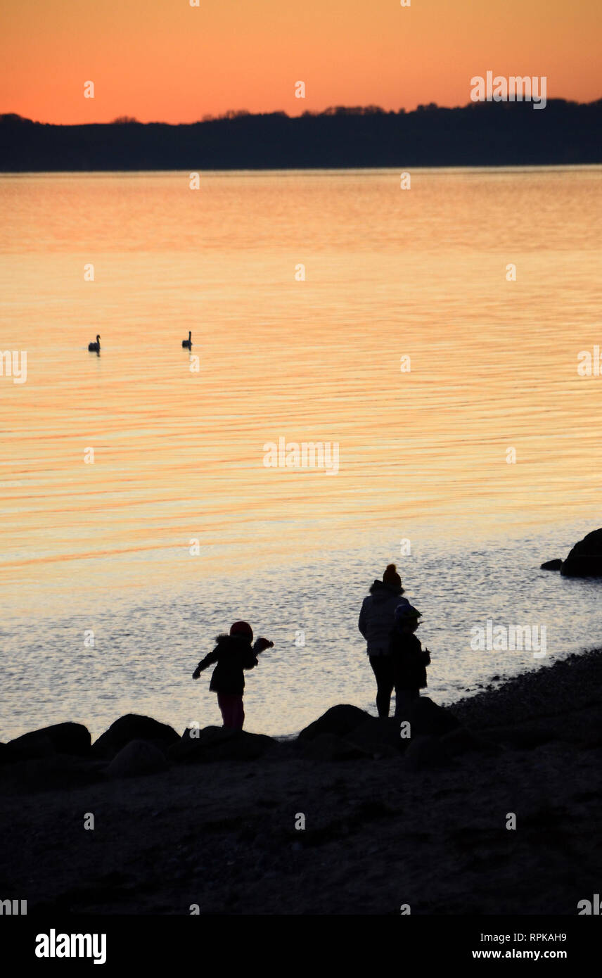 Sunset over the sea, people seen as black silhouettes towards the sea. Stock Photo
