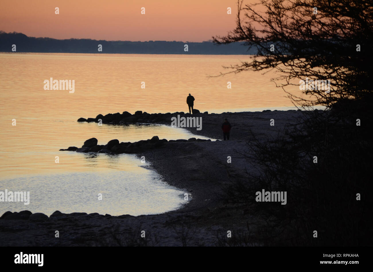 Sunset over the sea, people seen as black silhouettes towards the sea. Stock Photo