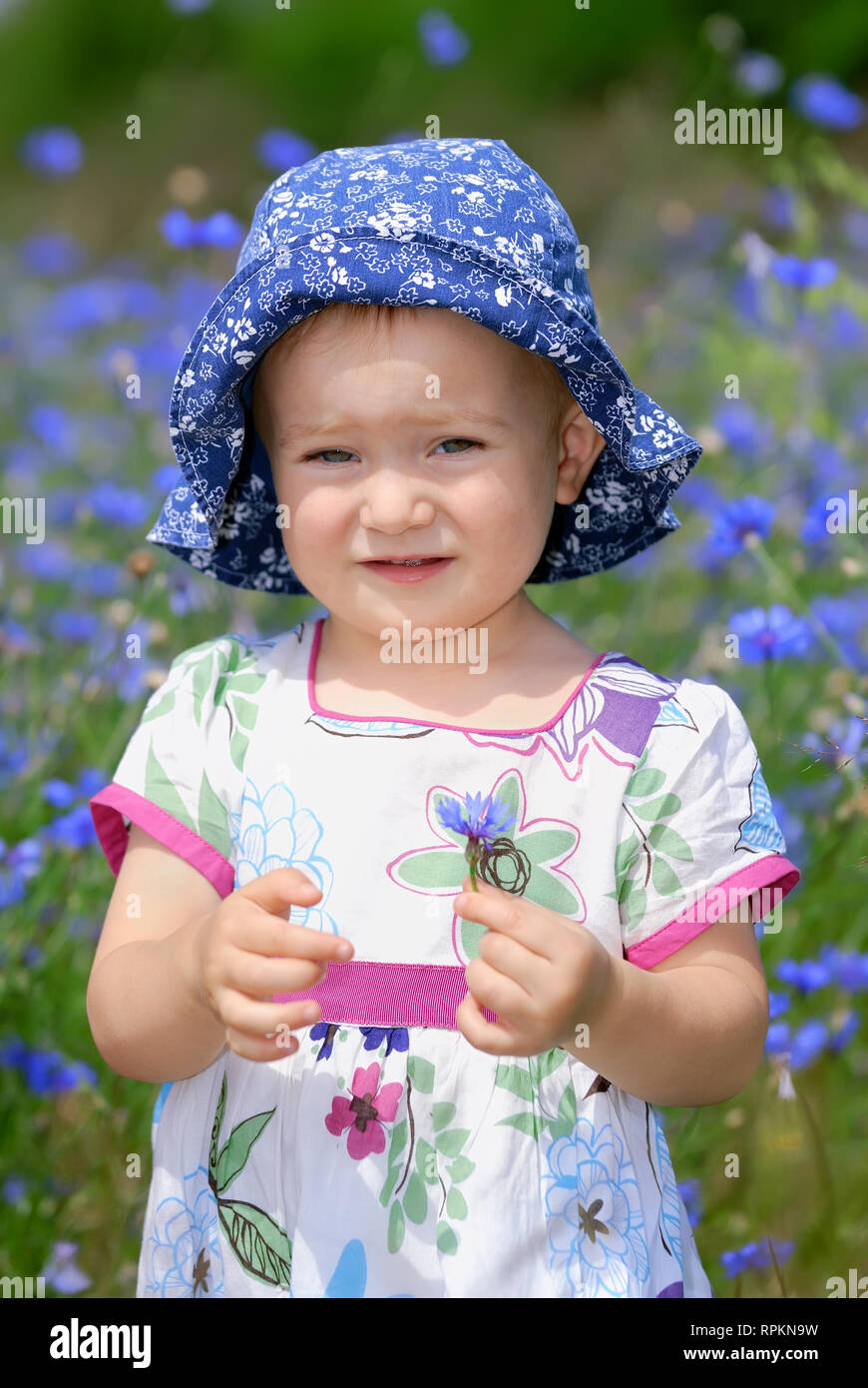 Cute little girl in a colorful dress and blue hat on flowery meadow Stock Photo