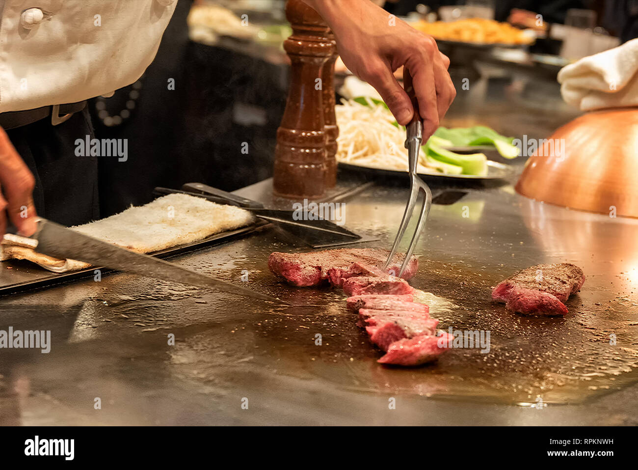 Chef at teppenyaki restaurant in Tokyo, Japan slicing Kobe beef on cooking surface Stock Photo