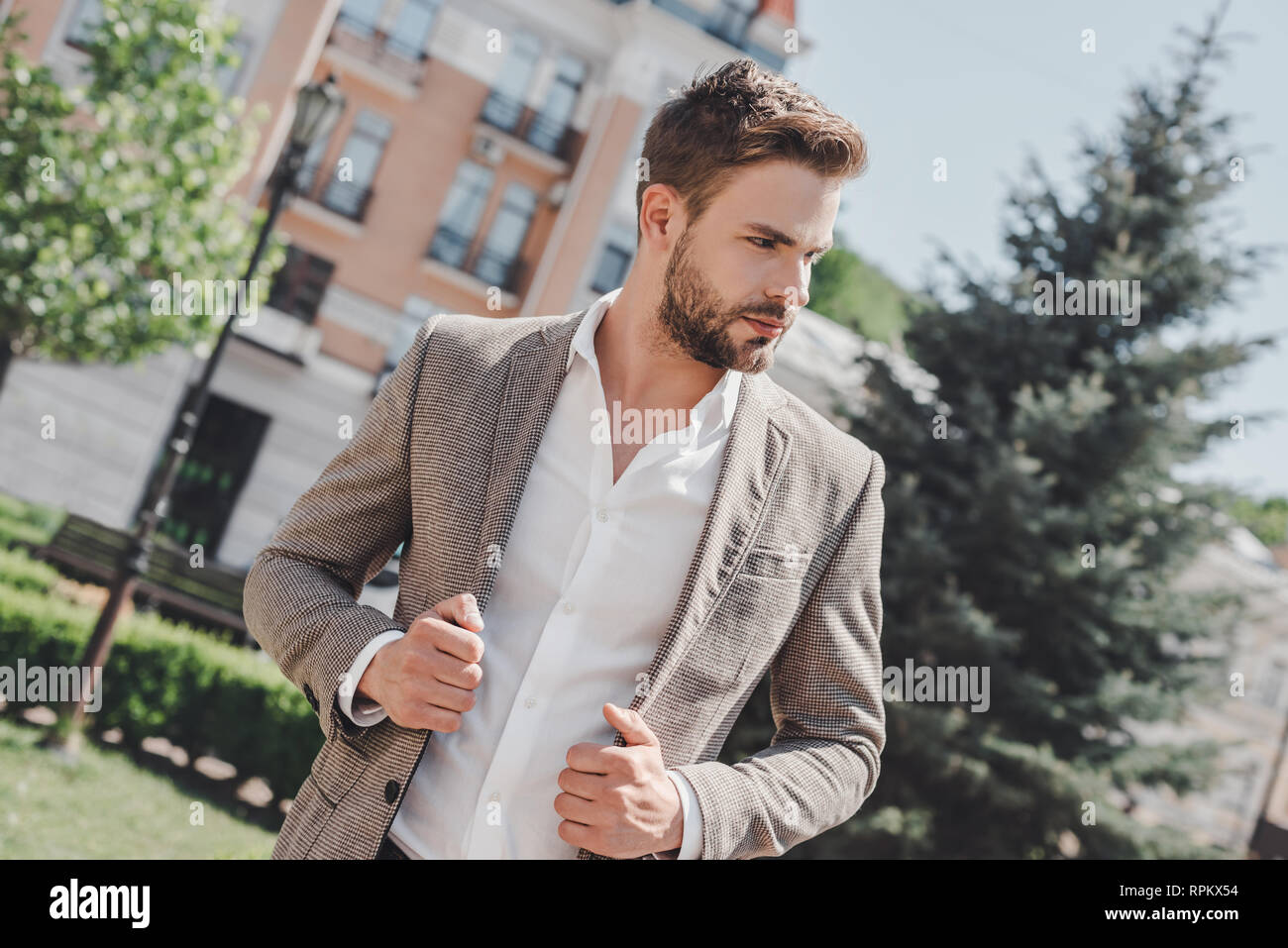 Handsome young businessman walking on city street in the morning going to work in office wear smart casual outfit of brown jacket and white shirt. Urban lifestyle of young professionals. Stock Photo
