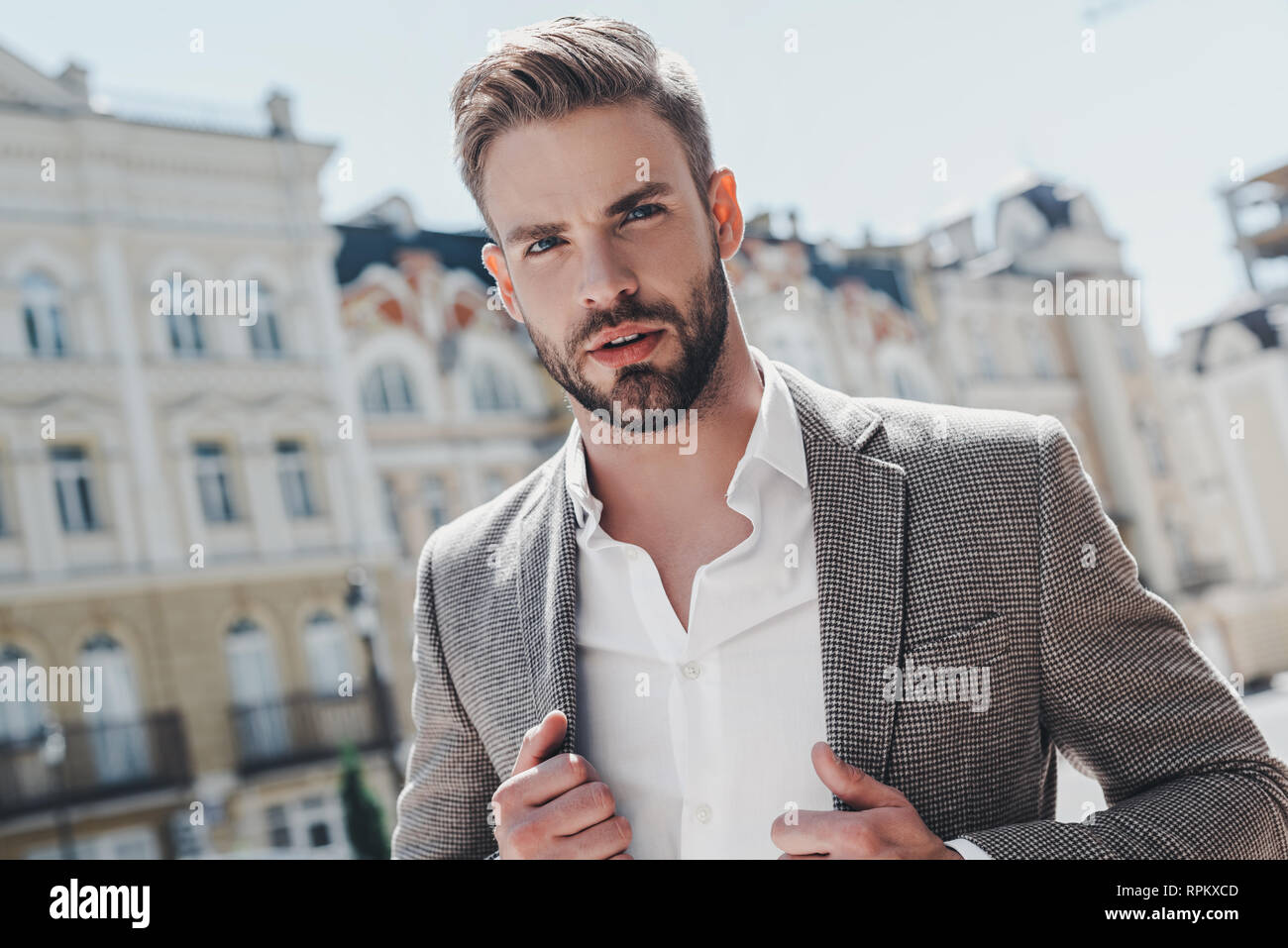 Handsome young businessman walking on city street. He is going to work in office wear smart casual outfit of brown jacket and white shirt. Urban lifestyle of young professionals. Stock Photo