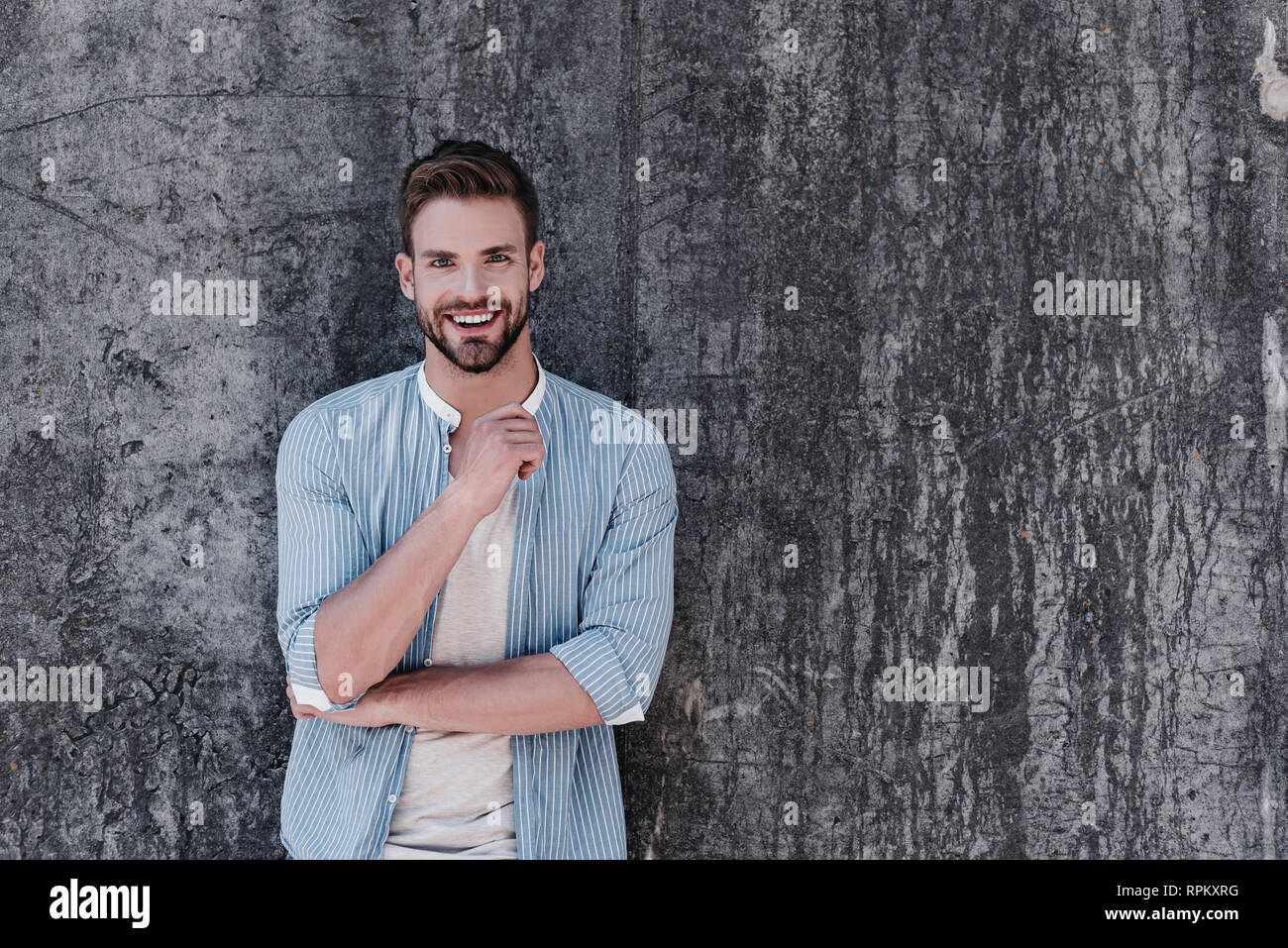 Happy young man dressed casually in blue stylish shirt and grey T-shirt, having a decisive attitude, smiling and looking at camera, isolated over grey background. Success concept Stock Photo