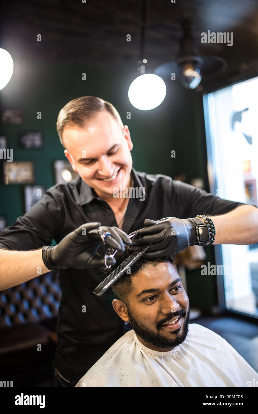 Hairdresser cuts hair, with scissors and black comb, on crown of
