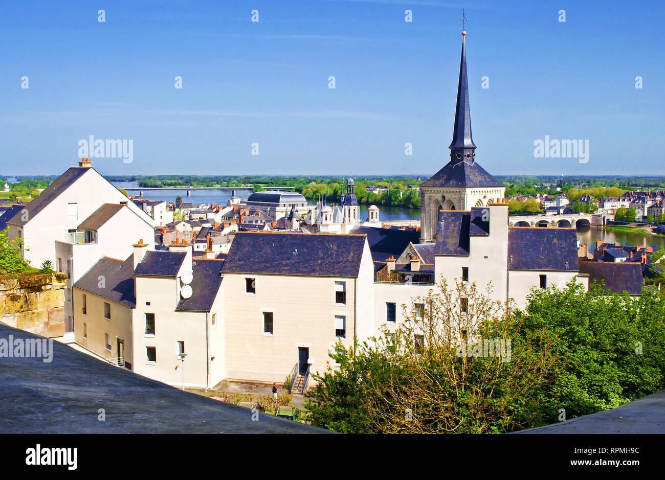Breathtaking view on amazing small town Saumur, France. Many white and gray houses near a Loire river, bridge, lots of green trees and rooftops. Warm  Stock Photo