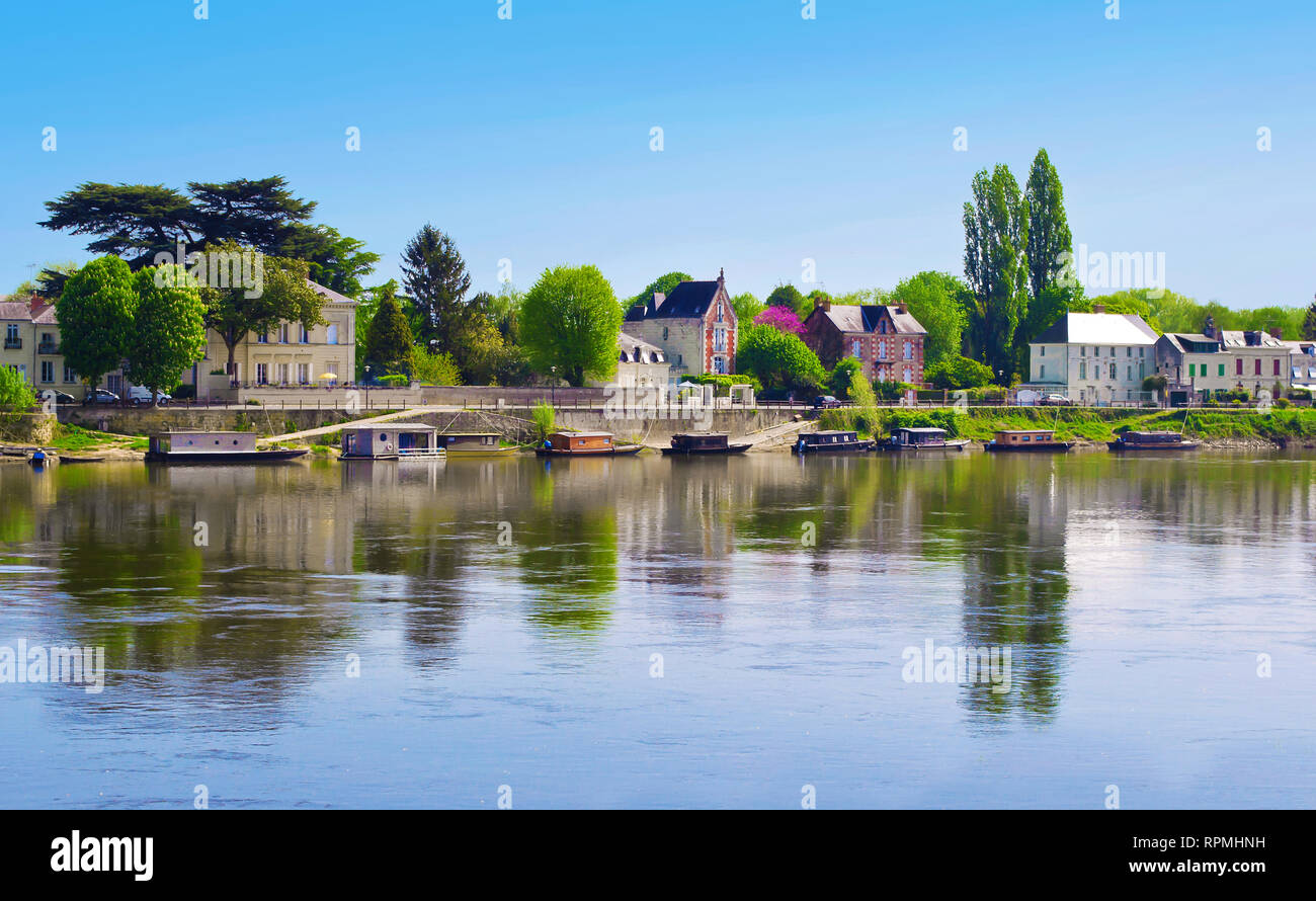 Breathtaking view on amazing small town Saumur, France. Many gray houses near Loire river, lots of green trees, a row of colorful boats. Warm spring m Stock Photo