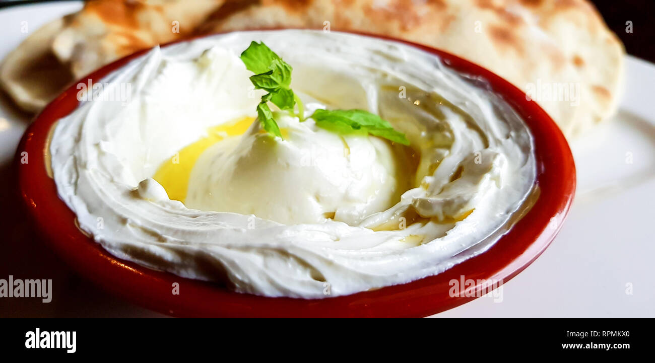A bowl of creamy Labneh, a thick Lebanese yoghurt dip with mint leaves and olive oil. Close up view of traditional Lebanese food in a restaurant. Stock Photo