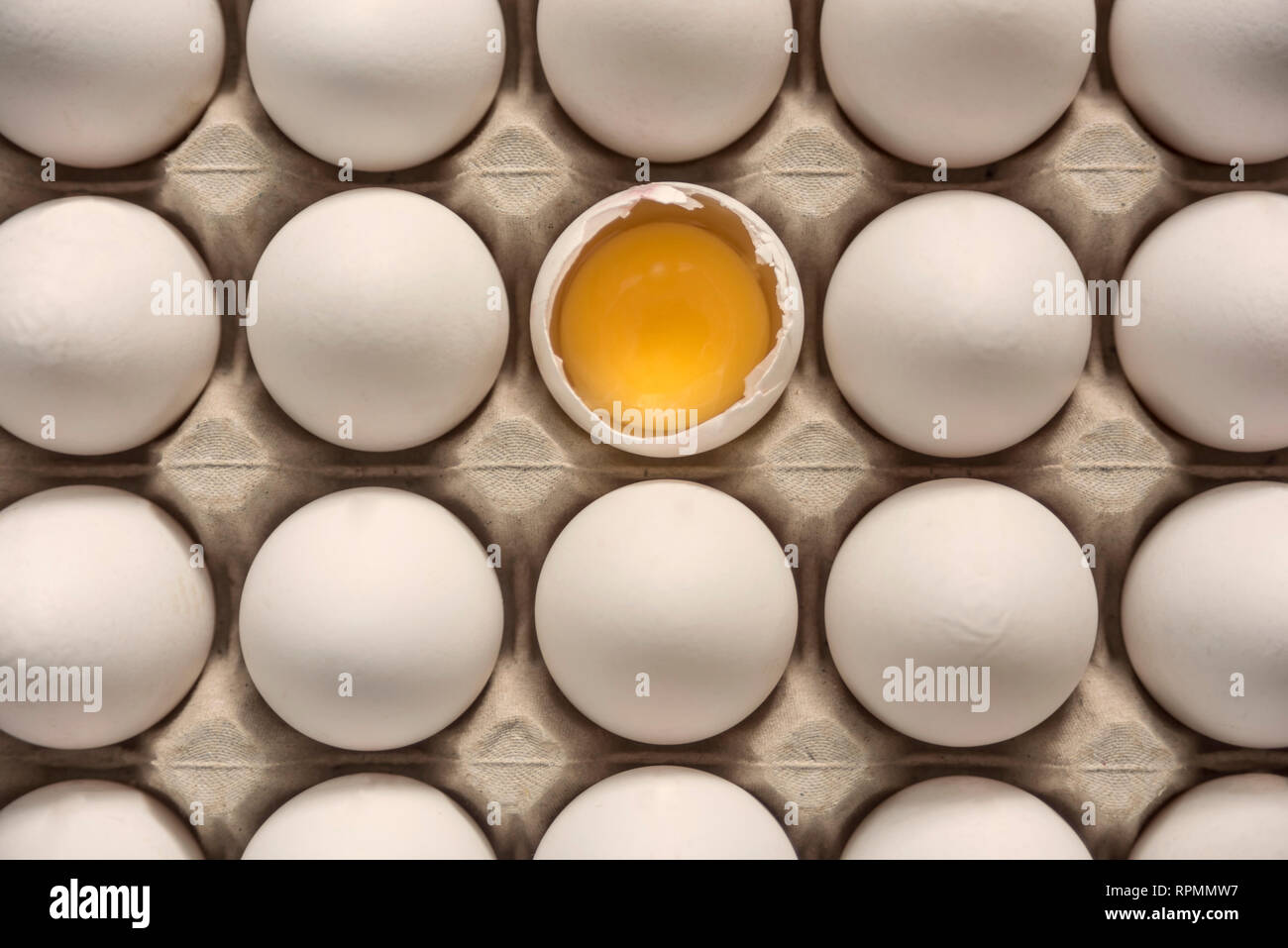 Many eggs in egg carton, one broken egg shell with visible egg yolk
