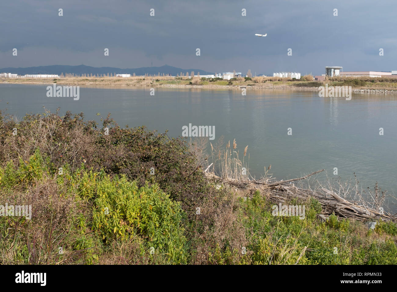 Llobregat River with industrial area in background while a plane prepares to land at Barcelona airport. Natural Areas of the Llobregat Delta. Spain. Stock Photo