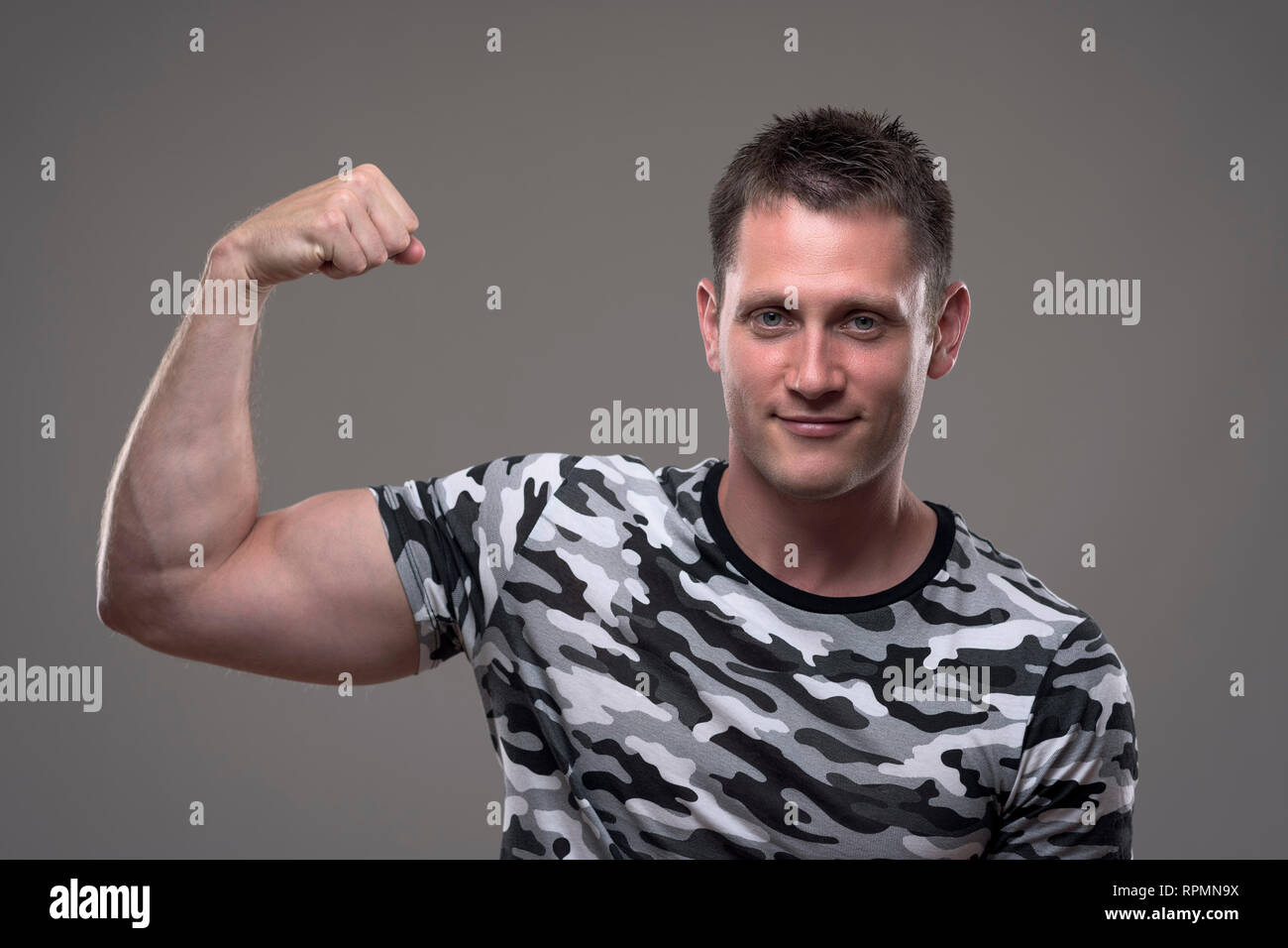 Portrait of athletic muscular fitness male model in army shirt flexing arm and showing bicep muscles. Stock Photo