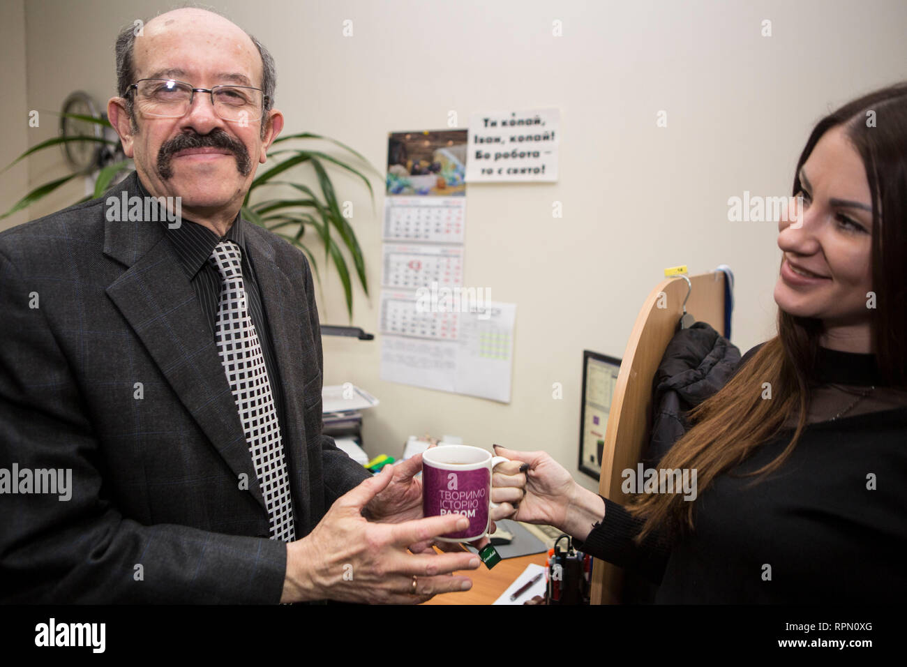 Young lady gives a cup of hot drink to older man with sympathy and smile, shows respect and cultural merits of Ukrainian society, man appreciates care Stock Photo