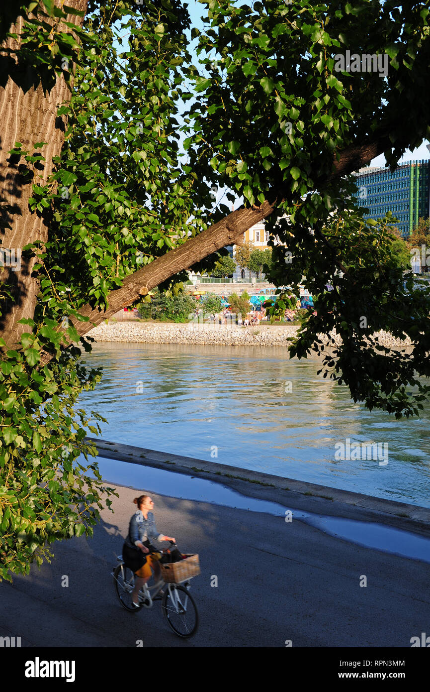 Young woman on a bicycle along the Donaukanal, Vienna, Austria. In the background, Herrmann Strandbar, Vienna's urban beach Stock Photo