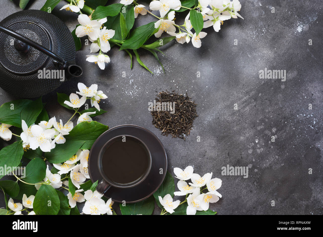 Green jasmin tea and jasmine flowers, cup of green tea on black. Top