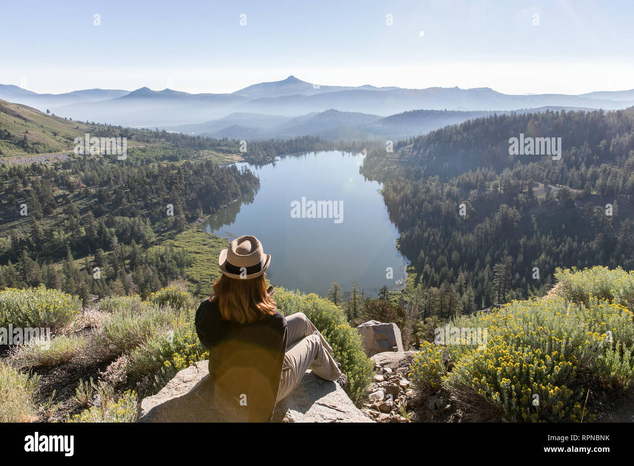 Woman in hat looking out over scenic lake in California Stock Photo