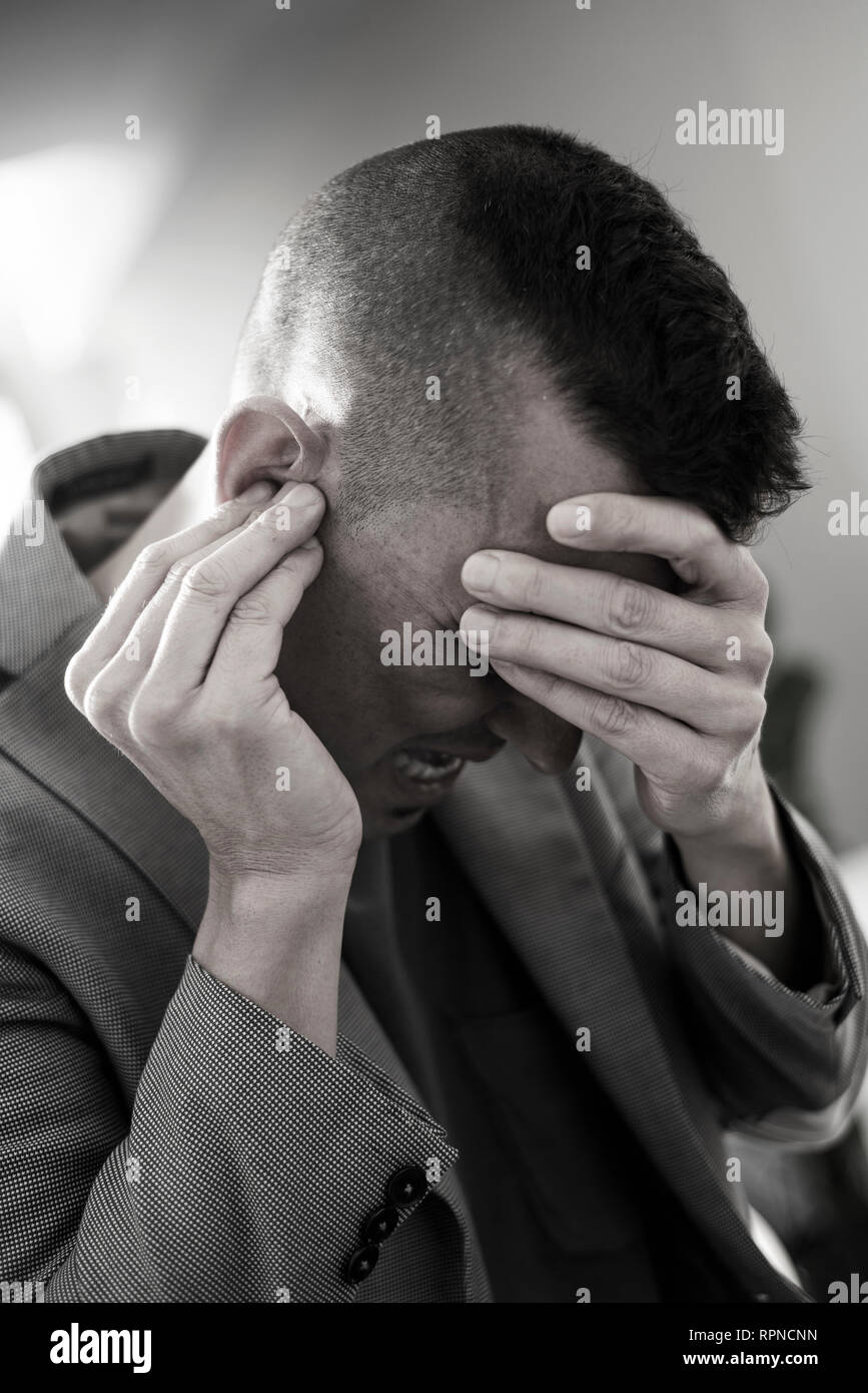 closeup of a suffering caucasian man with one hand in his head and the other hand covering his ear Stock Photo