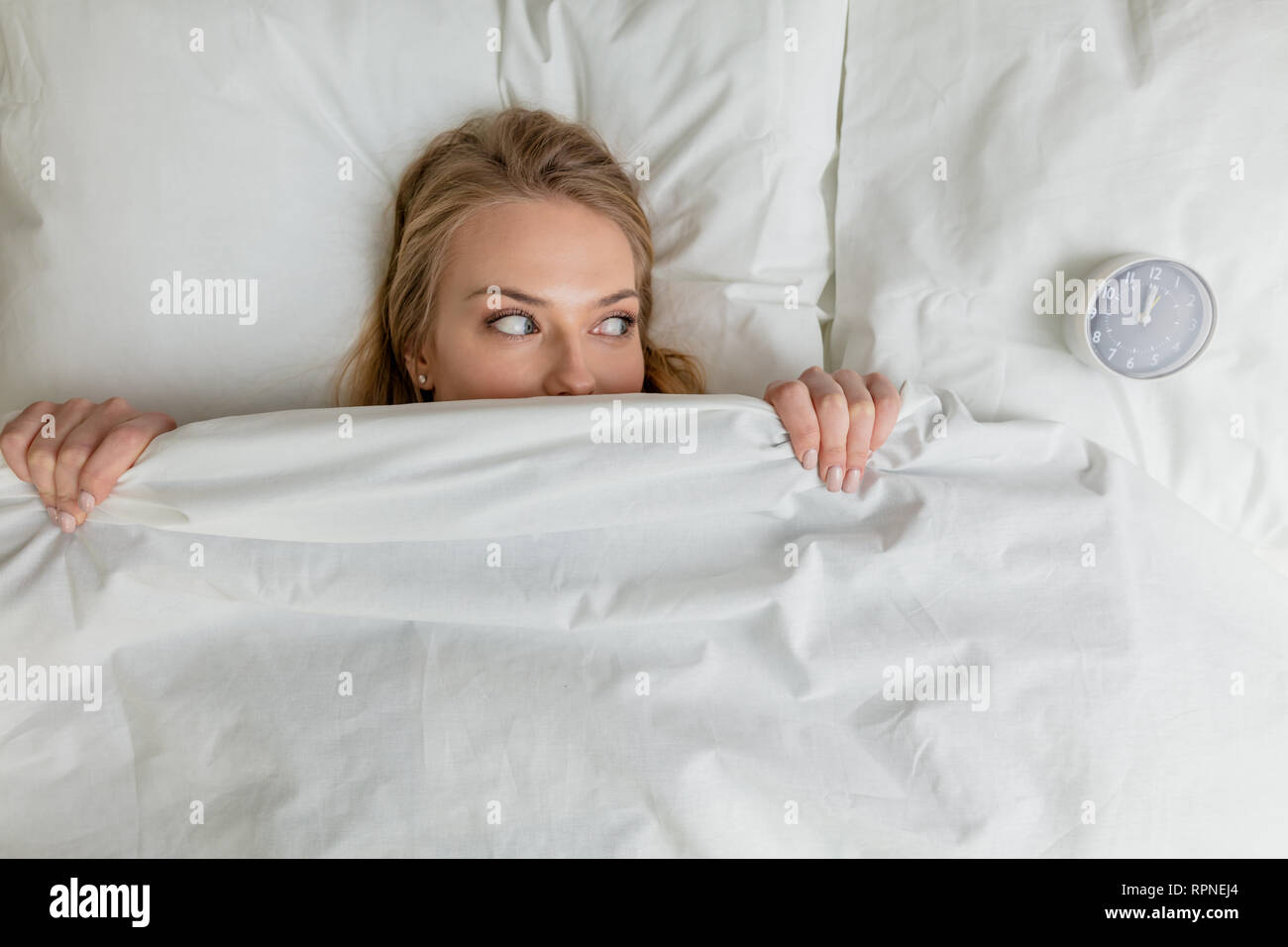 awesome girl is afraid of an alarm clock. close up top view photo. spare time, relaxation, fear