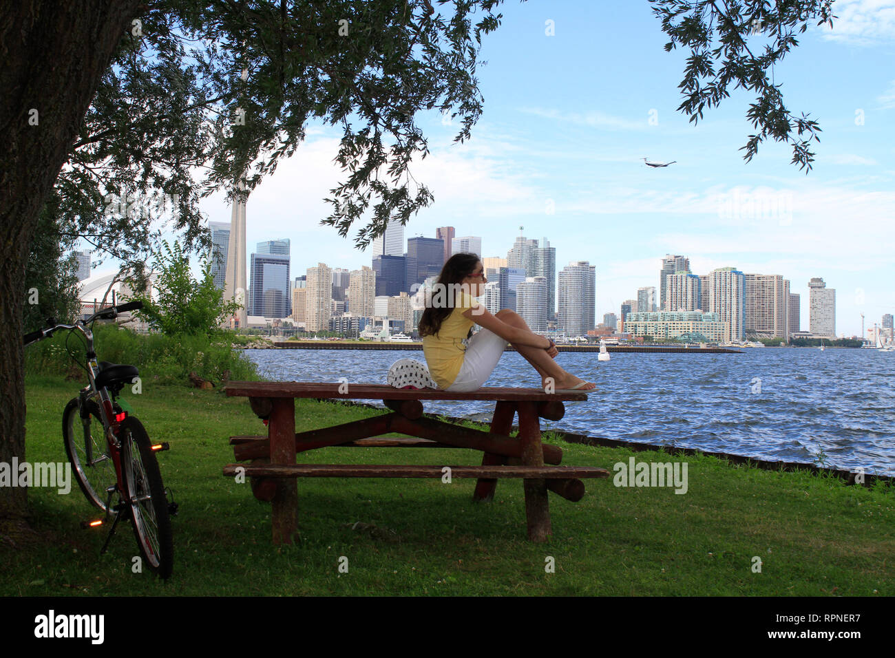 Ten year old girl sits on a park picnic table on Centre Island against a Toronto, Ontario cityscape in Canada. Stock Photo