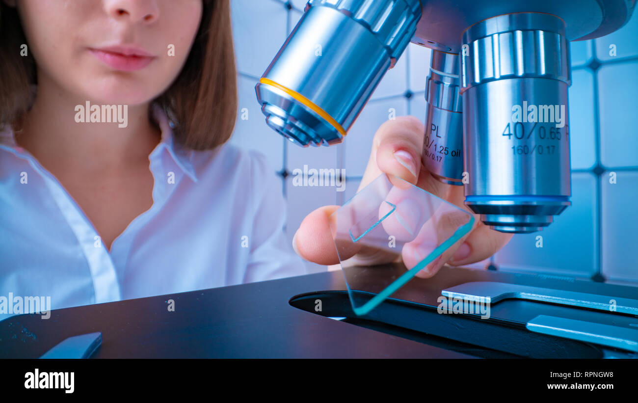 Scientist analyzing microscope slide at laboratory. Young woman technician is examining a histological sample, a biopsy in the laboratory of cancer re Stock Photo